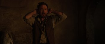 Movie still from “Brahms: The Boy II” (2020), directed by William Brent Bell – A man in a vest and tie holding his hands behind his ears; Close Up shot, Low angle