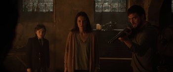 Movie still from “Brahms: The Boy II” (2020), directed by William Brent Bell – A woman standing in front of a window in a dark room; Medium shot, Over the shoulder angle