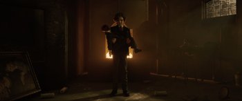 Movie still from “Brahms: The Boy II” (2020), directed by William Brent Bell – A man in a dark room holding an object in his hands; Wide shot, Low angle