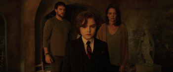 Movie still from “Brahms: The Boy II” (2020), directed by William Brent Bell – A boy in a suit and tie with two people behind him; Medium shot, Low angle