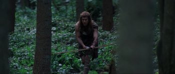 Movie still from “Braveheart” (1995), directed by Mel Gibson – A man with a long hair and a beard is holding a stick in the woods; Medium shot, Low angle