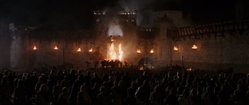 Movie still from “Braveheart” (1995), directed by Mel Gibson – A crowd of people standing around a burning building at night; Extreme Wide shot, High angle