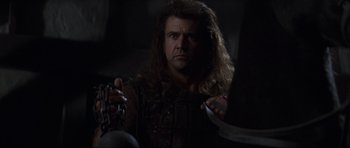 Movie still from “Braveheart” (1995), directed by Mel Gibson – A man with long hair holding a knife and fork; Close Up shot, Low angle