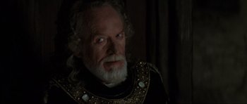 Movie still from “Braveheart” (1995), directed by Mel Gibson – An old man with a beard wearing a black and gold outfit; Close Up shot, Over the shoulder angle
