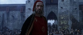 Movie still from “Braveheart” (1995), directed by Mel Gibson – A man in a red outfit standing in front of a castle; Medium shot, Over the shoulder angle