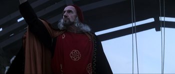 Movie still from “Braveheart” (1995), directed by Mel Gibson – A man with a long beard wearing a red and black costume; Medium shot, Low angle