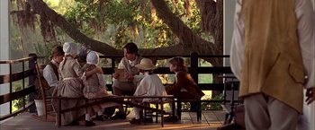 Movie still from “The Patriot” (2000), directed by Roland Emmerich – A group of people sitting on a bench under a tree; Wide shot, Over the shoulder angle