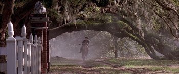 Movie still from “The Patriot” (2000), directed by Roland Emmerich – A man riding a horse down a dirt road under a tree; Extreme Wide shot, Low angle