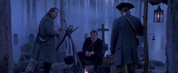 Movie still from “The Patriot” (2000), directed by Roland Emmerich – A man sitting in front of a cross and a fire pit; Wide shot, Over the shoulder angle