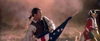 Movie still from “The Patriot” (2000), directed by Roland Emmerich – A man holding an american flag while standing on a hill; Medium shot, Low angle