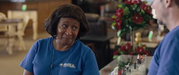 Movie still from “Breaking News in Yuba County” (2021), directed by Tate Taylor – An older woman sitting at a table in front of flowers; Close Up shot, Over the shoulder angle