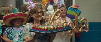 Movie still from “Breaking News in Yuba County” (2021), directed by Tate Taylor – A woman holding a birthday cake with candles on it; Medium shot, Over the shoulder angle