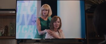 Movie still from “Breaking News in Yuba County” (2021), directed by Tate Taylor – A woman standing next to another woman in front of a tv; Medium shot, Over the shoulder angle