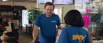 Movie still from “Breaking News in Yuba County” (2021), directed by Tate Taylor – A man standing next to a woman in front of a television; Medium shot, Over the shoulder angle