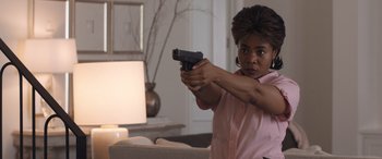 Movie still from “Breaking News in Yuba County” (2021), directed by Tate Taylor – A woman holding a gun in a living room; Medium shot, Over the shoulder angle