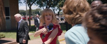 Movie still from “Breaking News in Yuba County” (2021), directed by Tate Taylor – A woman in a red dress is holding a microphone; Medium shot, Over the shoulder angle