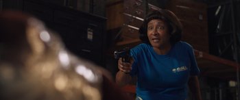 Movie still from “Breaking News in Yuba County” (2021), directed by Tate Taylor – A woman holding a gun in a room with cabinets; Medium shot, Over the shoulder angle