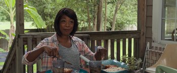 Movie still from “Breaking News in Yuba County” (2021), directed by Tate Taylor – A woman sitting at a table with a plate of food; Medium shot, Over the shoulder angle