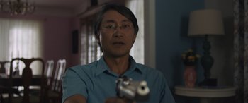 Movie still from “Breaking News in Yuba County” (2021), directed by Tate Taylor – A man holding a gun while wearing glasses and a blue shirt; Close Up shot, Over the shoulder angle