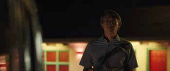 Movie still from “Breaking News in Yuba County” (2021), directed by Tate Taylor – A man standing in front of a building at night holding a flashlight; Medium shot, Low angle