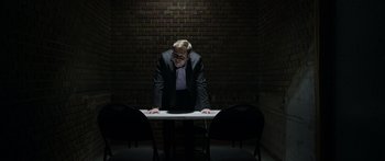 Movie still from “Broken” (2021), directed by Patrick Phillips – A man standing at a table in front of a brick wall; Medium shot, Over the shoulder angle