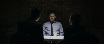 Movie still from “Broken” (2021), directed by Patrick Phillips – A man sitting at a table in front of two other people; Medium shot, Over the shoulder angle