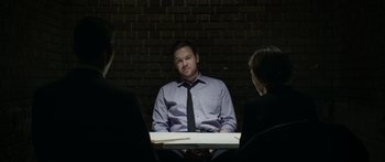 Movie still from “Broken” (2021), directed by Patrick Phillips – A man sitting at a table in front of two other people; Medium shot, Over the shoulder angle