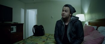 Movie still from “Broken” (2021), directed by Patrick Phillips – A man sitting on a bed in a room with a bag; Close Up shot, Over the shoulder angle