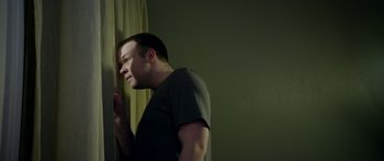 Movie still from “Broken” (2021), directed by Patrick Phillips – A man standing next to a curtain in a room; Close Up shot, Low angle