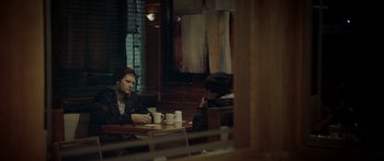 Movie still from “Broken” (2021), directed by Patrick Phillips – Two people sitting at a table with cups of coffee; Medium shot, Over the shoulder angle