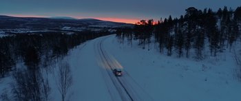 Movie still from “Broken” (2021), directed by Patrick Phillips – A car driving down a snow covered road at sunset; Extreme Wide shot, High angle