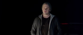 Movie still from “Broken” (2021), directed by Patrick Phillips – A man wearing a hat and a black jacket; Medium shot, Low angle