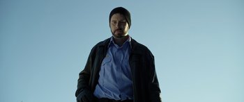 Movie still from “Broken” (2021), directed by Patrick Phillips – A man wearing a black hat and a blue shirt; Medium shot, Low angle