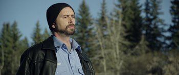 Movie still from “Broken” (2021), directed by Patrick Phillips – A man with a beard wearing a black hat and jacket; Close Up shot, Over the shoulder angle