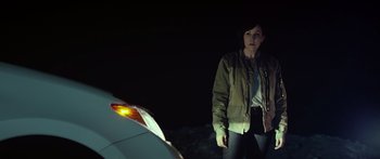 Movie still from “Broken” (2021), directed by Patrick Phillips – A woman standing in front of a car at night; Medium shot, Over the shoulder angle