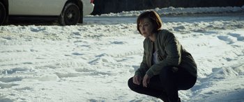 Movie still from “Broken” (2021), directed by Patrick Phillips – A woman crouching down in the snow near a car; Medium shot, High angle