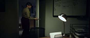 Movie still from “Broken” (2021), directed by Patrick Phillips – A woman standing in front of a desk with a lamp; Medium shot, Over the shoulder angle