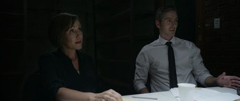 Movie still from “Broken” (2021), directed by Patrick Phillips – A man and a woman sitting at a table in a dark room; Medium shot, Over the shoulder angle