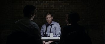 Movie still from “Broken” (2021), directed by Patrick Phillips – A man sitting in front of two other men; Medium shot, Over the shoulder angle