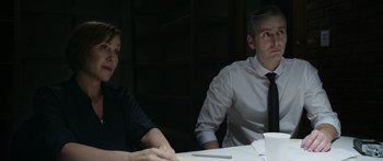 Movie still from “Broken” (2021), directed by Patrick Phillips – A man and a woman sitting at a table with papers in front of them; Medium shot, Over the shoulder angle
