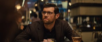 Movie still from “Bros” (2022), directed by Nicholas Stoller – A person sitting at a table with a glass; Close Up shot, Over the shoulder angle