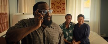 Movie still from “Bros” (2022), directed by Nicholas Stoller – A man talking on a cell phone in front of two other men; Medium shot, Over the shoulder angle