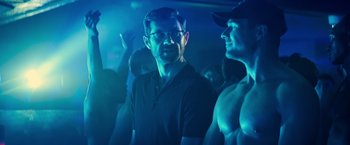 Movie still from “Bros” (2022), directed by Nicholas Stoller – A group of men standing in a dark room; Medium shot, Over the shoulder angle