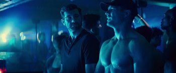 Movie still from “Bros” (2022), directed by Nicholas Stoller – A man standing next to another man in a dark room; Medium shot, Over the shoulder angle