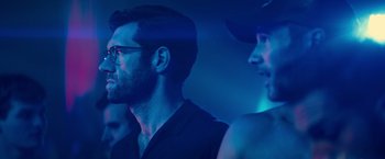 Movie still from “Bros” (2022), directed by Nicholas Stoller – A man with a beard and glasses in a dark room; Close Up shot, Over the shoulder angle