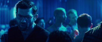 Movie still from “Bros” (2022), directed by Nicholas Stoller – A group of people in a dark room with blue lighting; Close Up shot, Over the shoulder angle