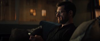 Movie still from “Bros” (2022), directed by Nicholas Stoller – A man sitting on a couch holding a cell phone; Close Up shot, Over the shoulder angle
