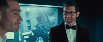 Movie still from “Bros” (2022), directed by Nicholas Stoller – A man in a suit and bow tie standing in front of a picture; Close Up shot, Over the shoulder angle
