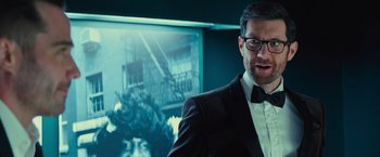 Movie still from “Bros” (2022), directed by Nicholas Stoller – A man wearing a suit and bow tie in front of a picture; Close Up shot, Over the shoulder angle