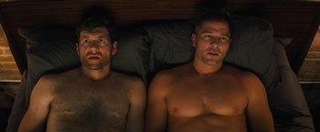 Movie still from “Bros” (2022), directed by Nicholas Stoller – Two shirtless men laying in a bed next to each other; Medium shot, Overhead angle